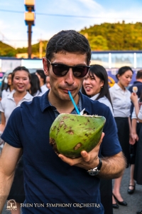 ココナッツに直接ストローをさして新鮮なジュースを飲むアシスタント・コンサートマスターのアルセン・ケティキアン。熱帯の島・台湾を訪れたら必ず味わいたい飲み物。海辺のサービスエリアにて。
